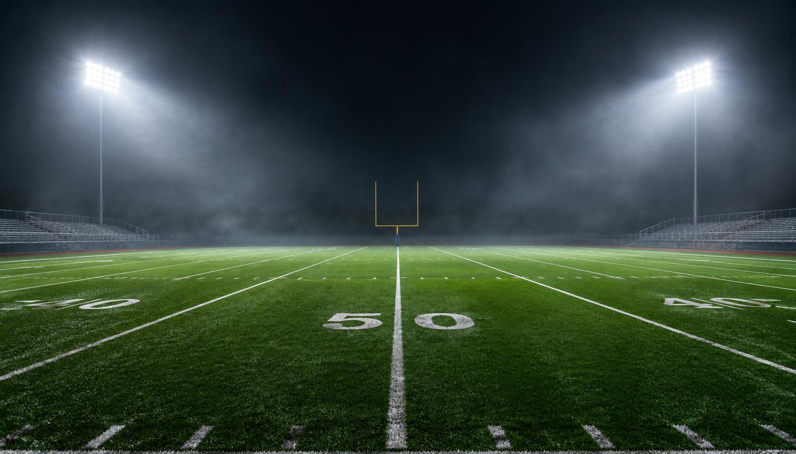 High school football field glowing under Friday night stadium lights